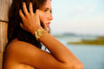 Woman with a gold botanical bracelet leaning against a wooden post by a body of water.