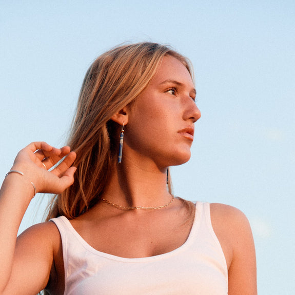 Woman wearing lapis earrings and blue jeans against a clear sky