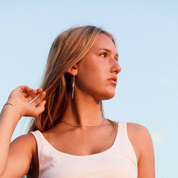 Woman wearing lapis earrings and blue jeans against a clear sky
